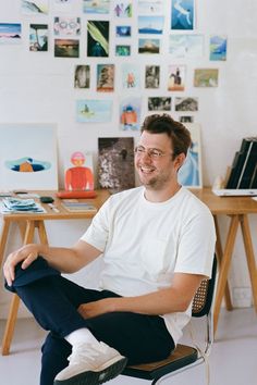 a man sitting on top of a chair in front of a desk with pictures on the wall