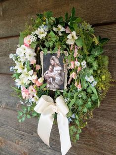 a wreath with flowers and a photo hanging on the side of a wooden wall next to a white ribbon