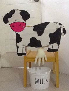 a wooden chair with a cow painted on it and a white bucket next to it