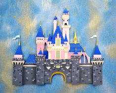 the castle is made out of paper and has blue turrets on its roof, while pink towers are in the background