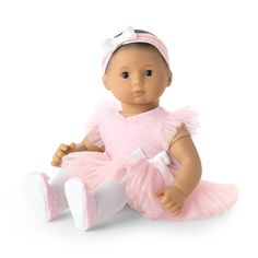 a baby doll sitting on the ground wearing a pink dress