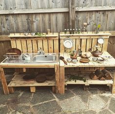 an outdoor kitchen made out of pallets and wooden crates with dishes on them, sitting next to a fence