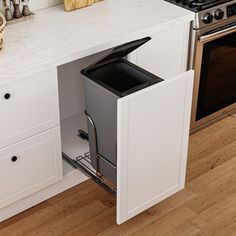 a kitchen with white cabinets and an open trash can in the middle of the cabinet