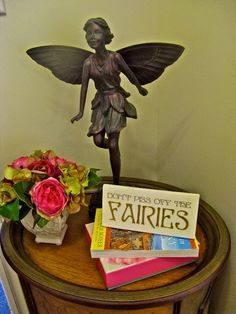 there is a small statue on top of a table with flowers and books next to it