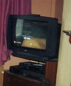 an old television sitting on top of a wooden stand in front of a purple curtain