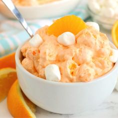 a bowl filled with orange fluff and marshmallows next to an orange slice