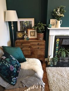 a living room with dark green walls and lots of plants on the fireplace mantel