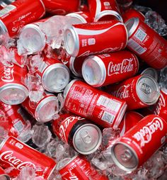 a pile of coca - cola cans sitting on top of ice