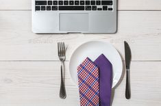 a white plate topped with a purple and blue tie next to a silver laptop computer