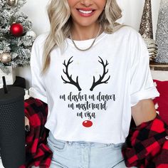 Get into the holiday spirit with a hilarious twist on a classic Christmas saying! This funny Christmas t-shirt features the phrase "On Dasher, On Dancer, On Mastercard, On Visa" with a cute graphic of festive reindeer horns and a red nose. Perfect for those who love to shop 'til they drop during the holiday season, this tee brings humor and style together. WHY YOU'LL LOVE THIS SHIRT: Festive & Funny: The clever play on Santa's reindeer names combined with credit cards adds a fun, modern touch to your holiday wardrobe. Cute Holiday Graphic: Reindeer antlers and a red nose give this shirt an extra dose of festive cheer. Perfect for Shoppers: A must-have for anyone who enjoys holiday shopping, gift-giving, or simply loves a good laugh. Soft & Comfortable: Made from premium quality material th Reindeer Horns, Reindeer Names, Santa's Reindeer, Reindeer Shirt, Funny Christmas Tshirts, Reindeer Antlers, Funny Christmas Shirts, Red Nose, Holiday Wardrobe