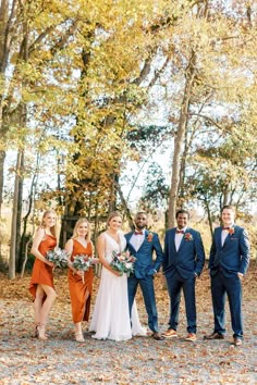 a group of people standing next to each other in front of trees with leaves on the ground