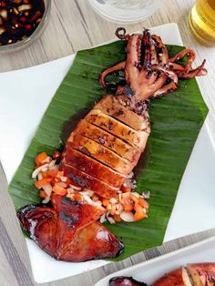 an octopus is on a banana leaf with other food items and drinks in the background