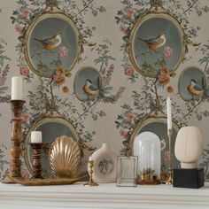 a mantle topped with candles and vases next to wallpaper