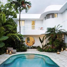 an outdoor swimming pool surrounded by palm trees and candles in front of a white house