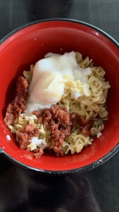 a red bowl filled with noodles and meat on top of a black table next to a fork