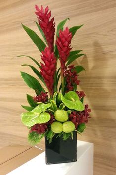 a black vase with red flowers and green leaves