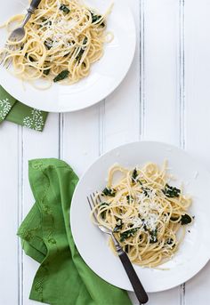 two plates of pasta with spinach and parmesan cheese on them, next to a green napkin