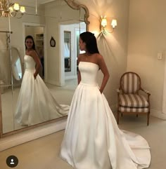 a woman standing in front of a mirror wearing a white wedding dress and looking at herself in the mirror