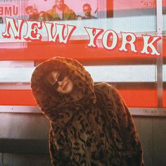 a woman wearing a leopard print coat in front of a new york sign