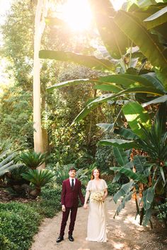 a bride and groom walking down a path in the woods