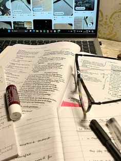 an open notebook sitting on top of a laptop computer next to a pen and glasses