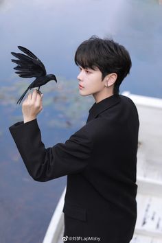 a person holding a bird in front of their face while standing next to a body of water