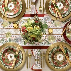 the table is set for christmas dinner with red and green plates, silverware, and gold cutlery