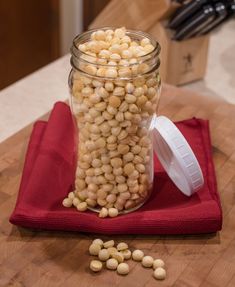 a jar filled with chickpeas sitting on top of a red cloth next to a knife