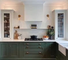 a kitchen with green cabinets and white counter tops is pictured in this image, there are bottles on the shelves above the stove