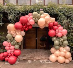 an arch made out of balloons in the middle of a courtyard with greenery on either side