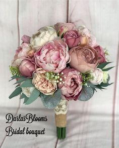 a bridal bouquet with pink flowers and greenery on a white wooden table top