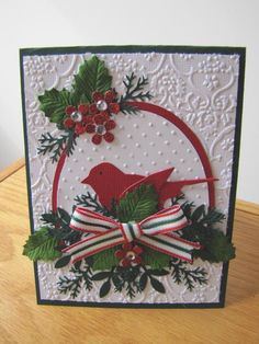 a christmas card with a red bird and holly wreath on it, sitting on top of a wooden table