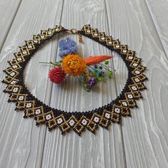 a beaded necklace with flowers in the center on a white wooden surface, hanging from a gold chain