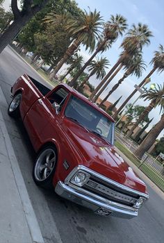 an old red car is parked on the side of the road next to palm trees