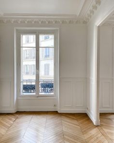 an empty room with wooden floors and white walls, in front of a window that looks out onto the street