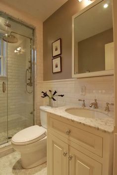 a white toilet sitting next to a walk in shower under a bathroom mirror with two framed pictures on the wall