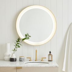 a bathroom vanity with a round mirror and gold faucet on the countertop