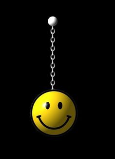 a smiley face hanging from a metal chain with two balls in the dark behind it