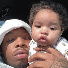 a man holding a baby in his arms while wearing a white hat and looking at the camera