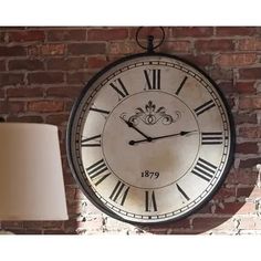 a large clock mounted to the side of a brick wall next to a lamp and lampshade