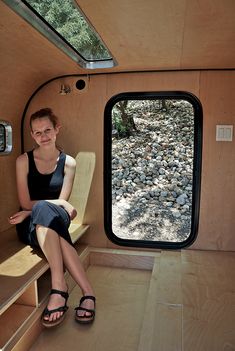 a woman is sitting on a bench in the back of a camper with its door open