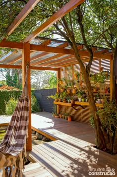 a hammock hanging from the side of a wooden deck with potted plants