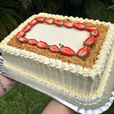 a person holding up a cake with strawberries on it