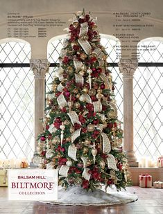 a decorated christmas tree with red and gold ornaments in a room next to large windows