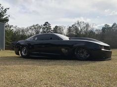 a black sports car parked on top of a grass covered field next to a metal structure