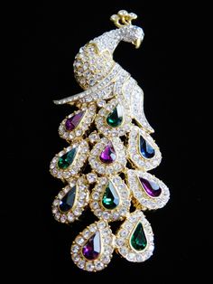 "Stunning, brilliant Nolan Miller goldtone large peacock brooch. This exquisite haute couture brooch showcases a stunning gold tone peacock encrusted with clear brilliant rhinestones which travel to his tail where his feathers hold emerald green, purple, and blue teardrops surrounded by more fabulous rhinestones. Measures 4\"L X 1 1/2\"W. Signed Nolan Miller, pristine condition. Perfect for Wedding, Anniversary, or Special Occasion wear." Elegant Peacock Design Brooch For Formal Occasions, Elegant Peacock Design Brooch For Formal Wear, Peacock Colored Wedding Brooch Jewelry, Elegant Party Brooch With Peacock Design, Elegant Peacock-colored Brooches For Wedding, Elegant Peacock Brooches For Wedding, Elegant Peacock Color Party Brooches, Elegant Peacock Color Wedding Brooches, Wedding Brooch With Peacock Design