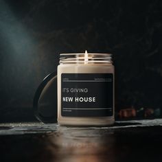 a candle is sitting on a table with the words it's giving new house