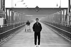 black and white photograph of man standing on bridge