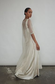 a woman standing in front of a white wall wearing a long dress with sheer sleeves