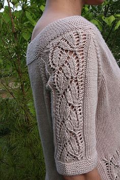 a woman with short hair wearing a sweater in front of some trees and bushes, looking off to the side